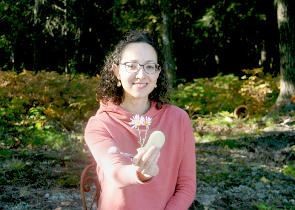 Smiling woman in nature presenting the tools used during an aesthetic acupuncture treatment.
